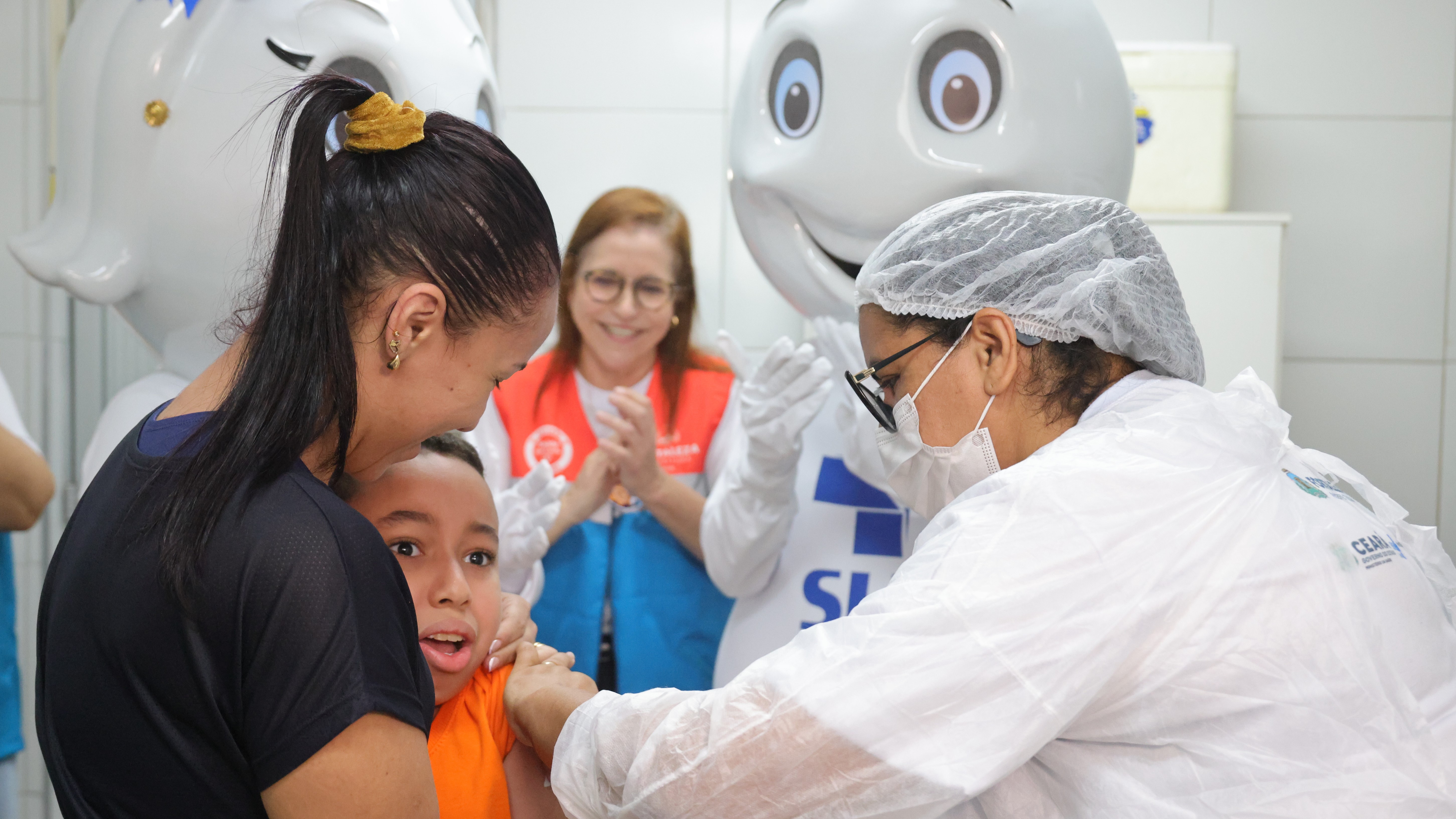 Enfermeira vacina um menino que está abraçado a mãe